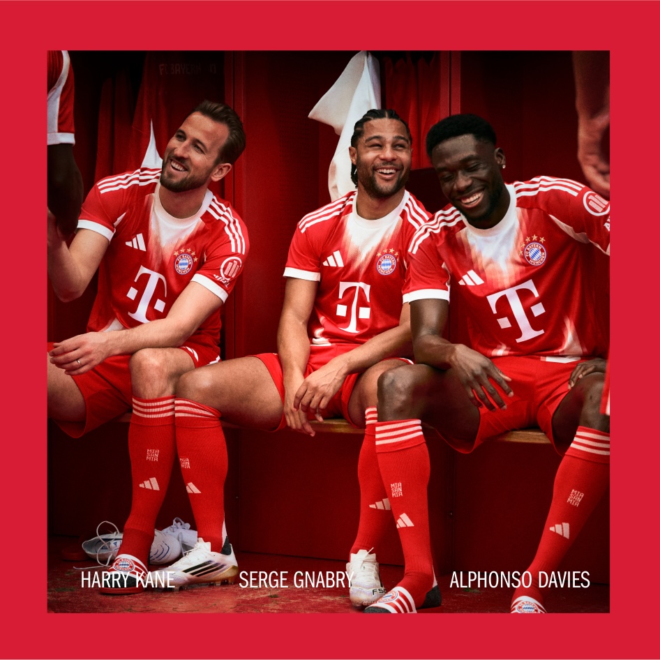 Drei Fußballspieler in roten Trikots sitzen zusammen, mit einem roten Vorhang oder Hintergrund.